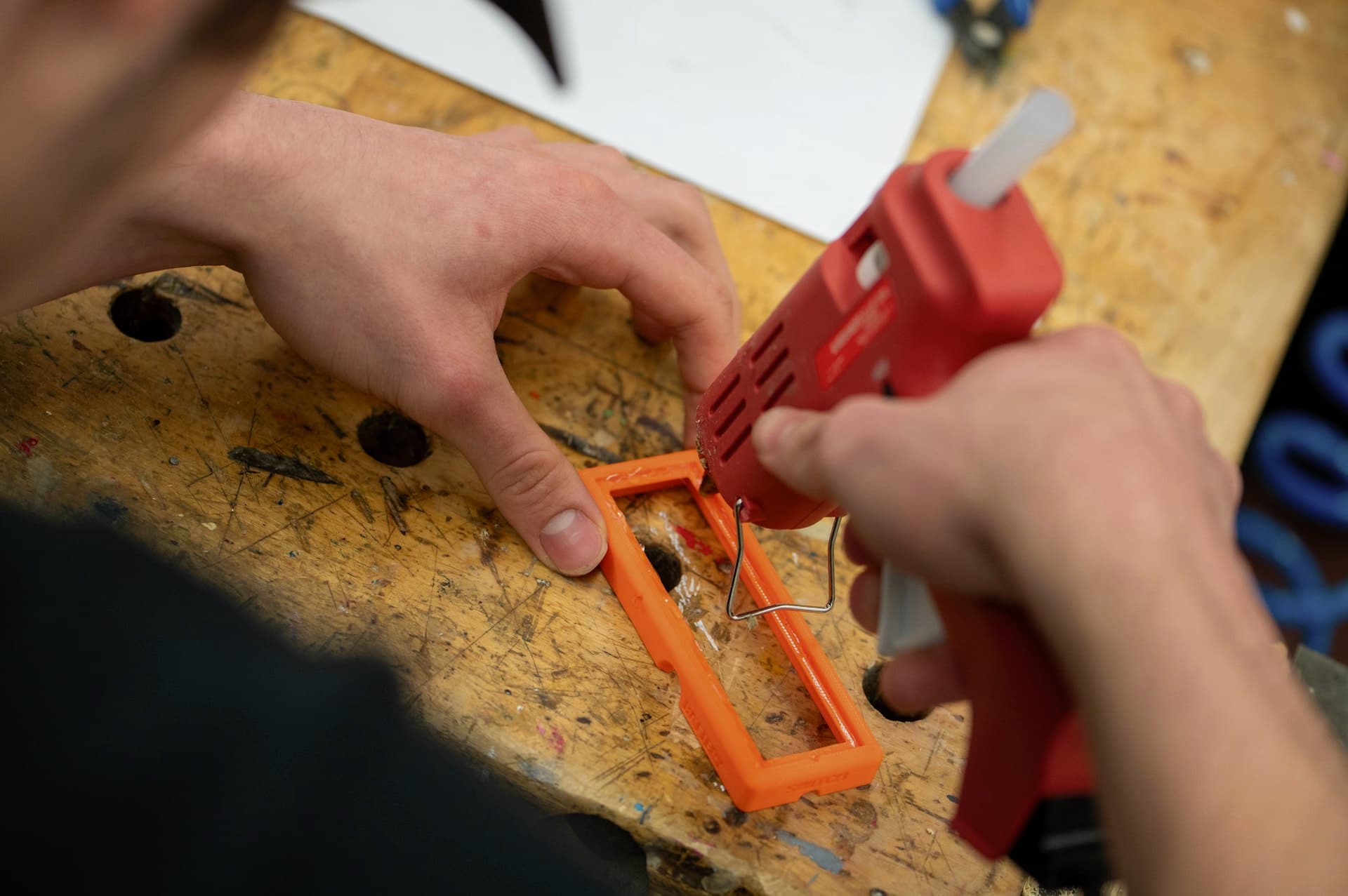 Manos aplicando adhesivo con una pistola de silicona caliente sobre una pieza de madera
